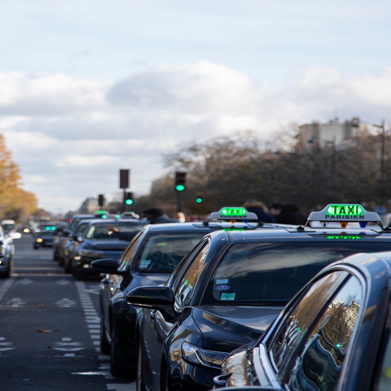 Taxis parisiens noirs alignés dans une rue, enseignes vertes TAXI PARISIEN allumées sous un ciel nuageux à Paris.