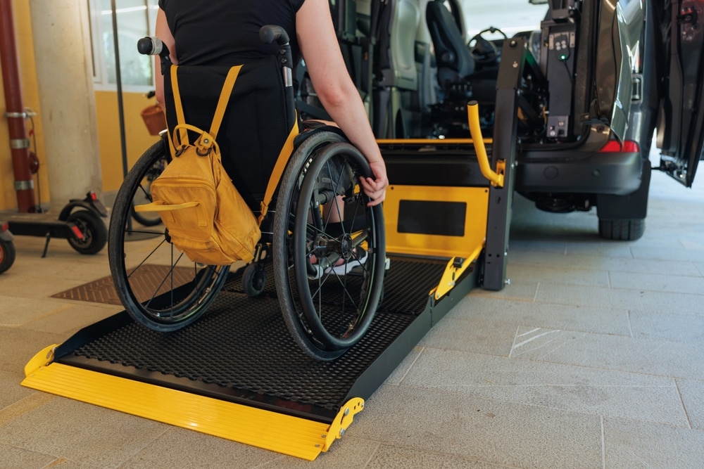 Accès véhicule adapté avec plateforme pour fauteuil roulant Femme en fauteuil roulant utilisant une plateforme élévatrice jaune pour monter dans un véhicule adapté.