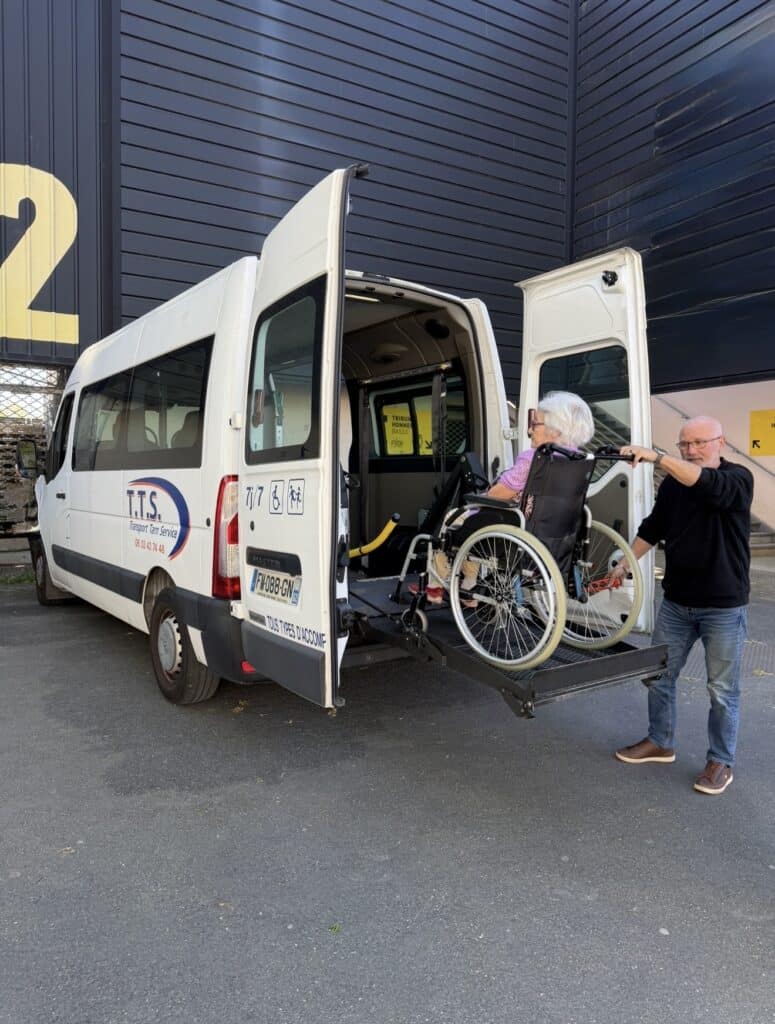 Transport Tarn Service : Transport PMR et Accessibilité Chauffeur aidant une dame en fauteuil roulant via le hayon élévateur d'un van TTS Transport Tarn Service.