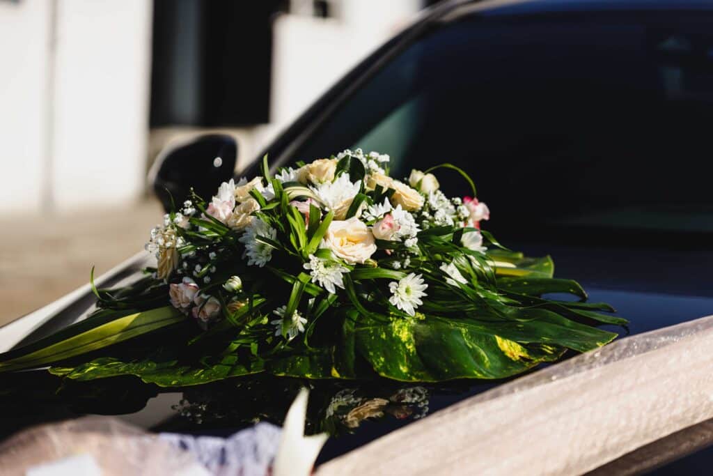Décoration Florale de Mariage : Roses Blanches sur Voiture Beautiful floral arrangement on a wedding car, featuring white and pink flowers with greenery, perfect for a wedding day.
